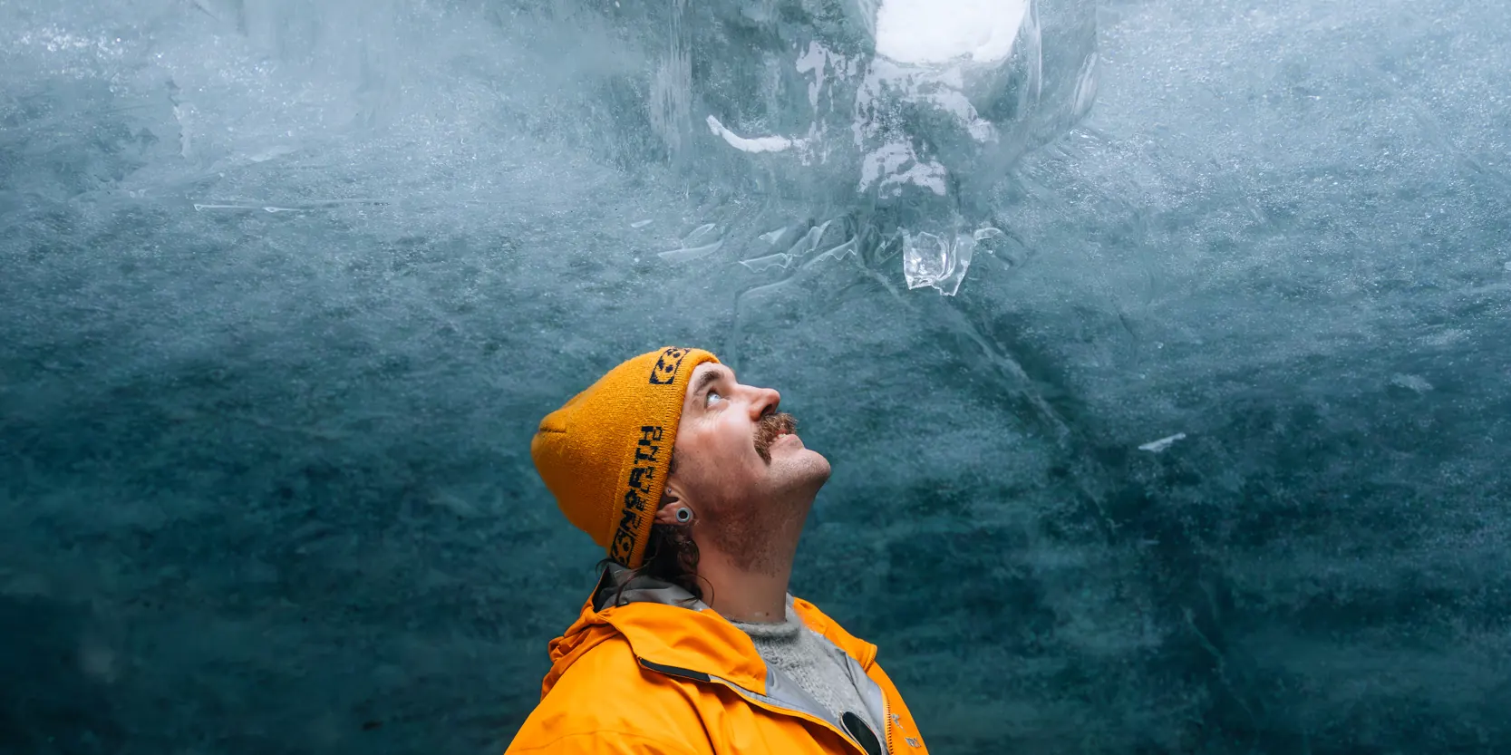 A guest looking up at the blue ice inside a glacier ice cave